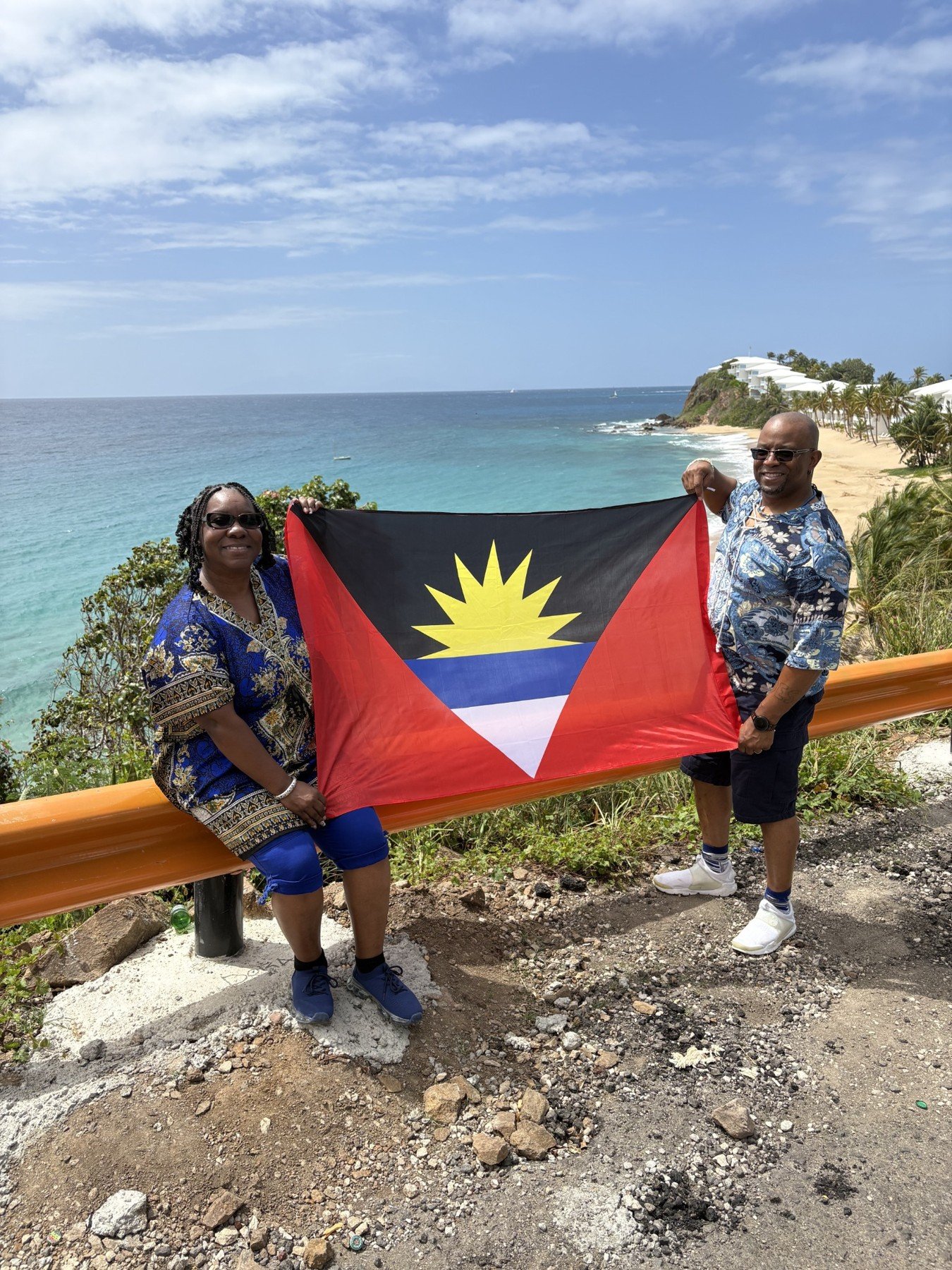 Two guests holding the Antigua and Barbuda flag with the beach and sea behind them