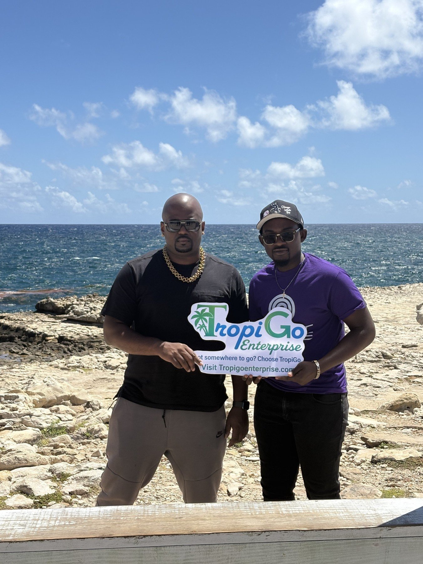 Ridge and a companion holding the TropiGo sign beside the coast