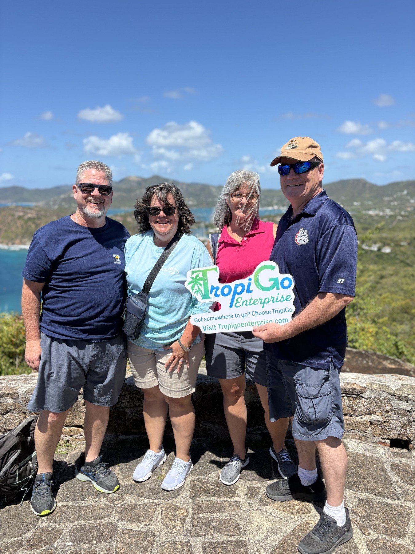 Four guests holding a TropiGo sign with a harbour view.